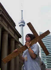 Een jongere uit Michigan (USA) draagt een kruis onder de bekende CN-tower in Toronto op weg naar een gebedsbijeenkomst.